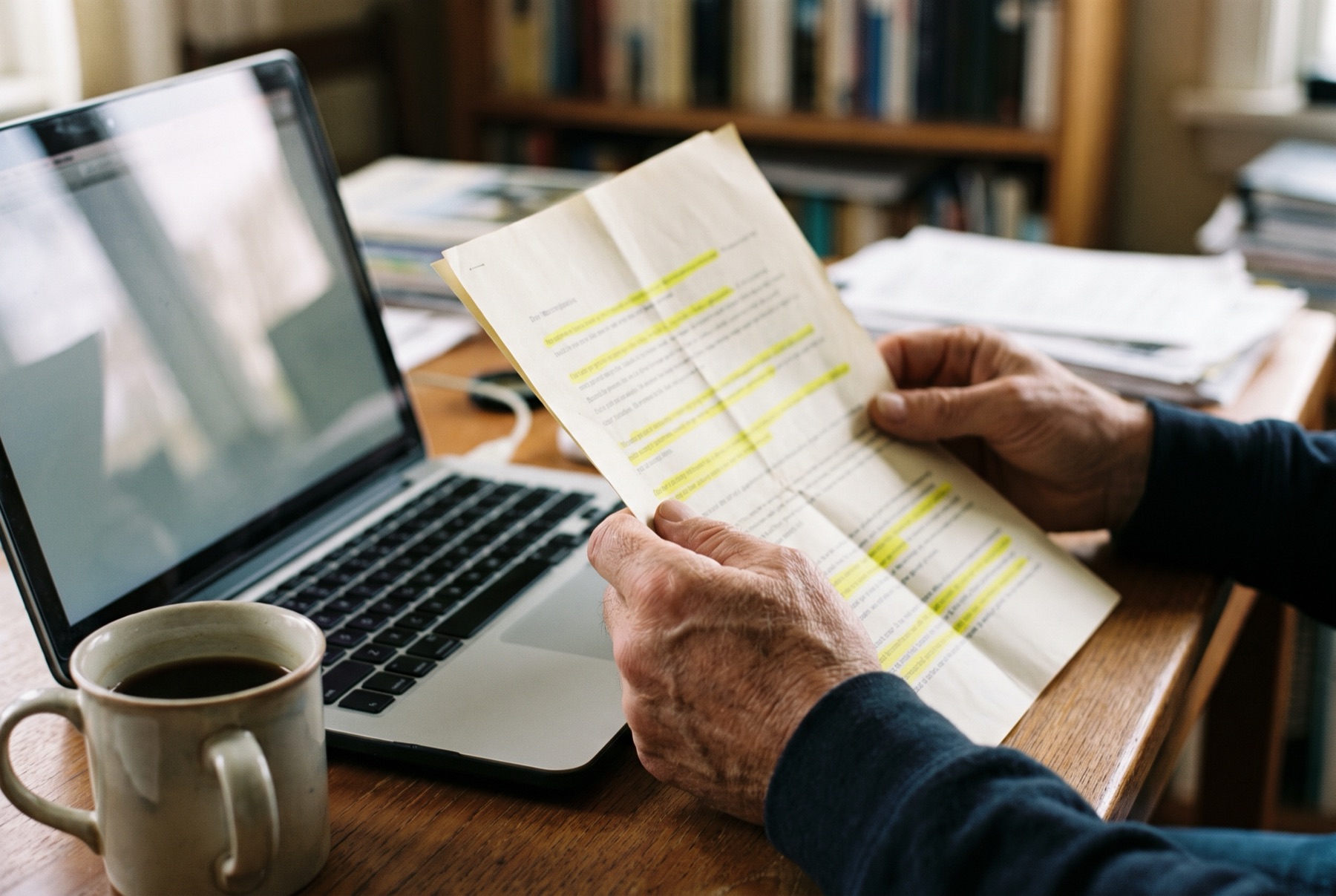 Close view of hands holding a folded credit report next to a laptop and a mug